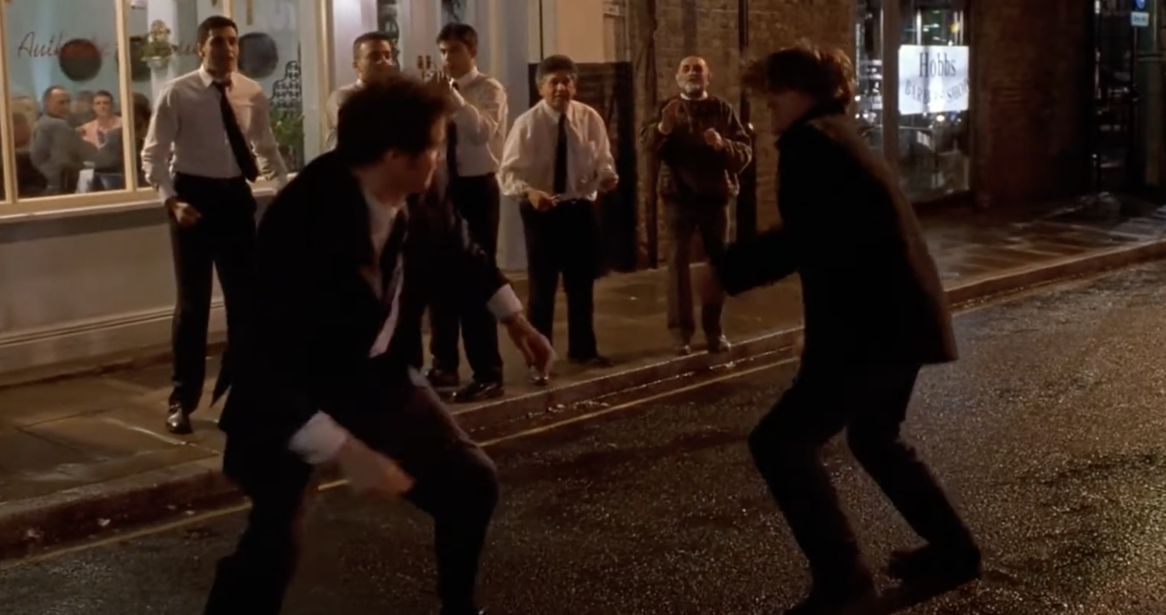 colin firth and hugh grant in the street facing each other ready to fight with people watching