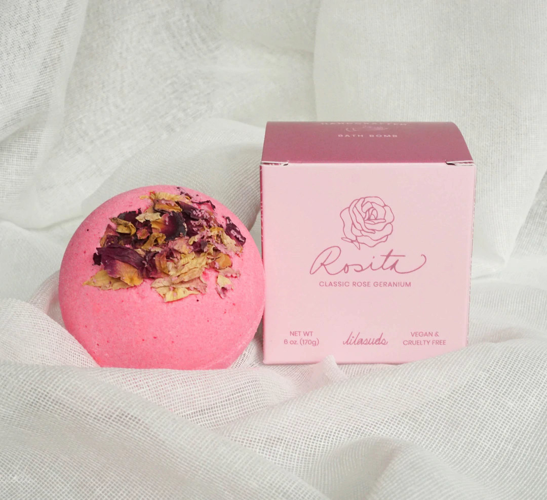 the pink bath bomb with dried flowers next to its box