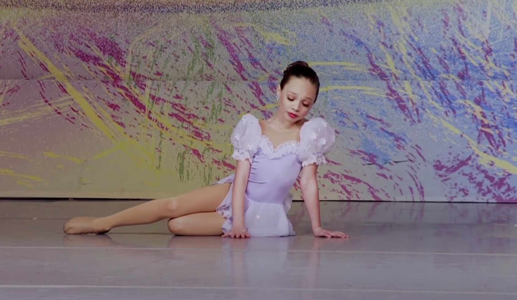 Maddie sitting on the floor in a dance outfit as a child