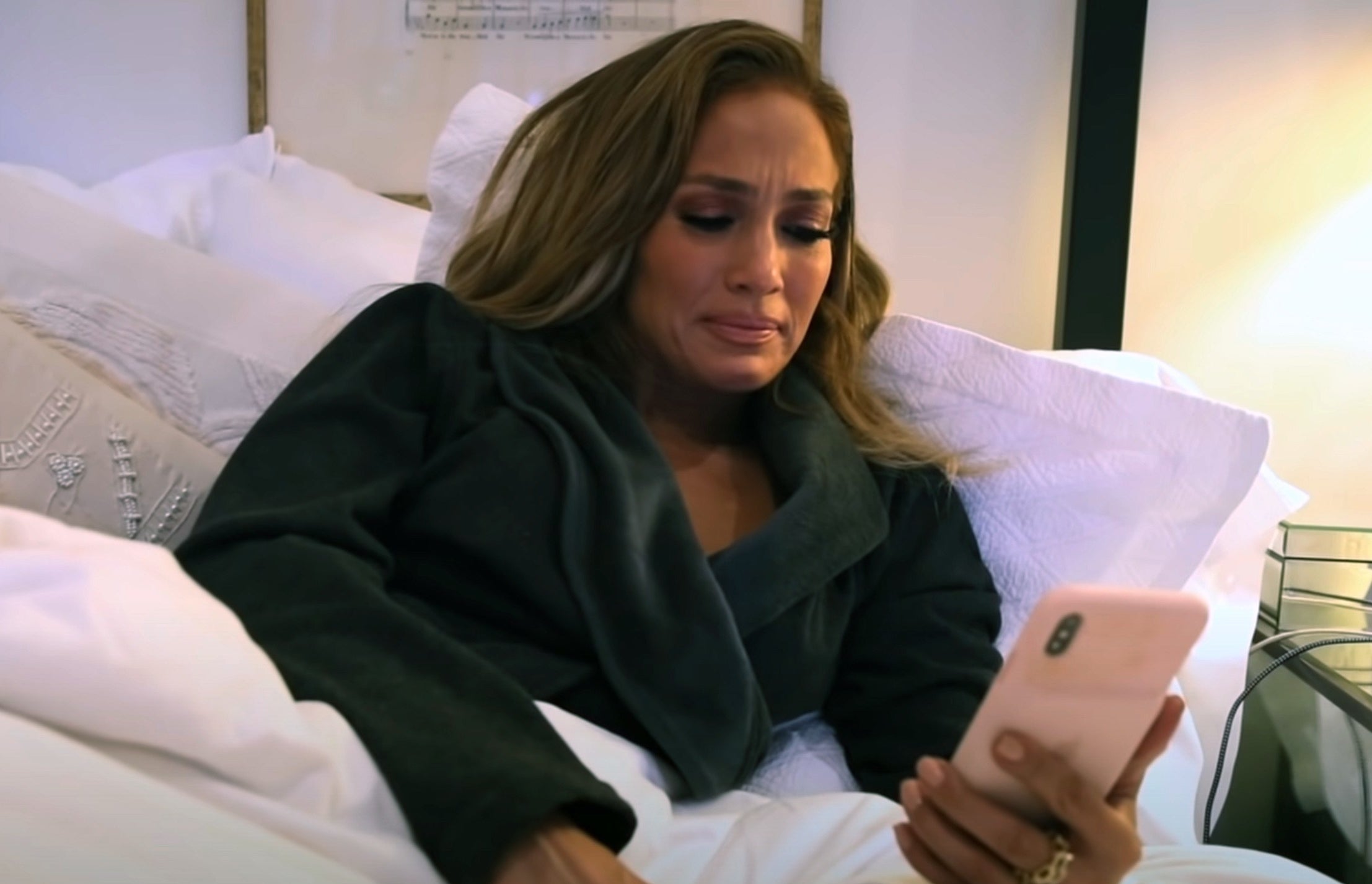Jennifer looks upset while looking at her phone in bed