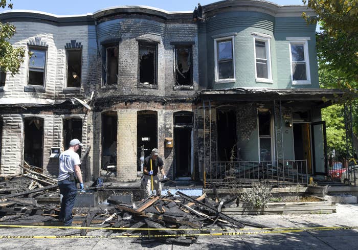 Two men sweep and survey debris from a fire in front of a charred row house