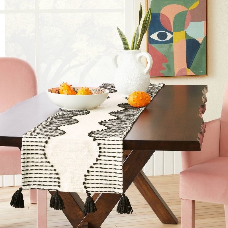 the knitted black and white runner on a wooden table with a bowl of kiwano fruit on top