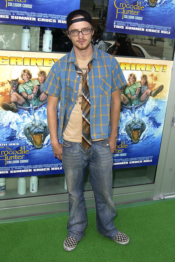 Aaron Paul in long baggy jeans, a backward cap, and multicolored tie, unbuttoned shirt, and T-shirt underneath