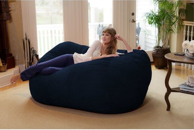 a person laying on a navy bean bag lounger placed in the living room