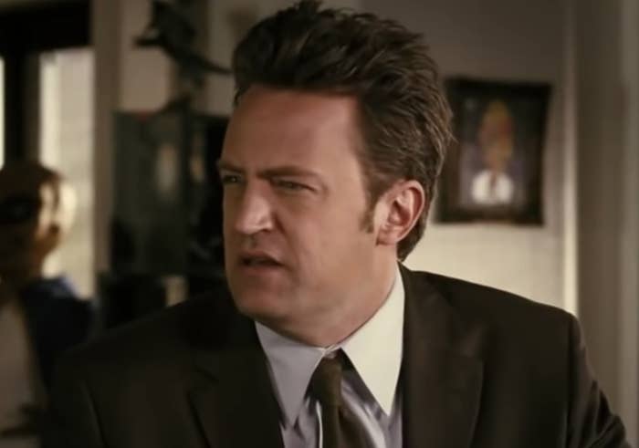 Matthew Perry sitting in a suit, glaring off-camera