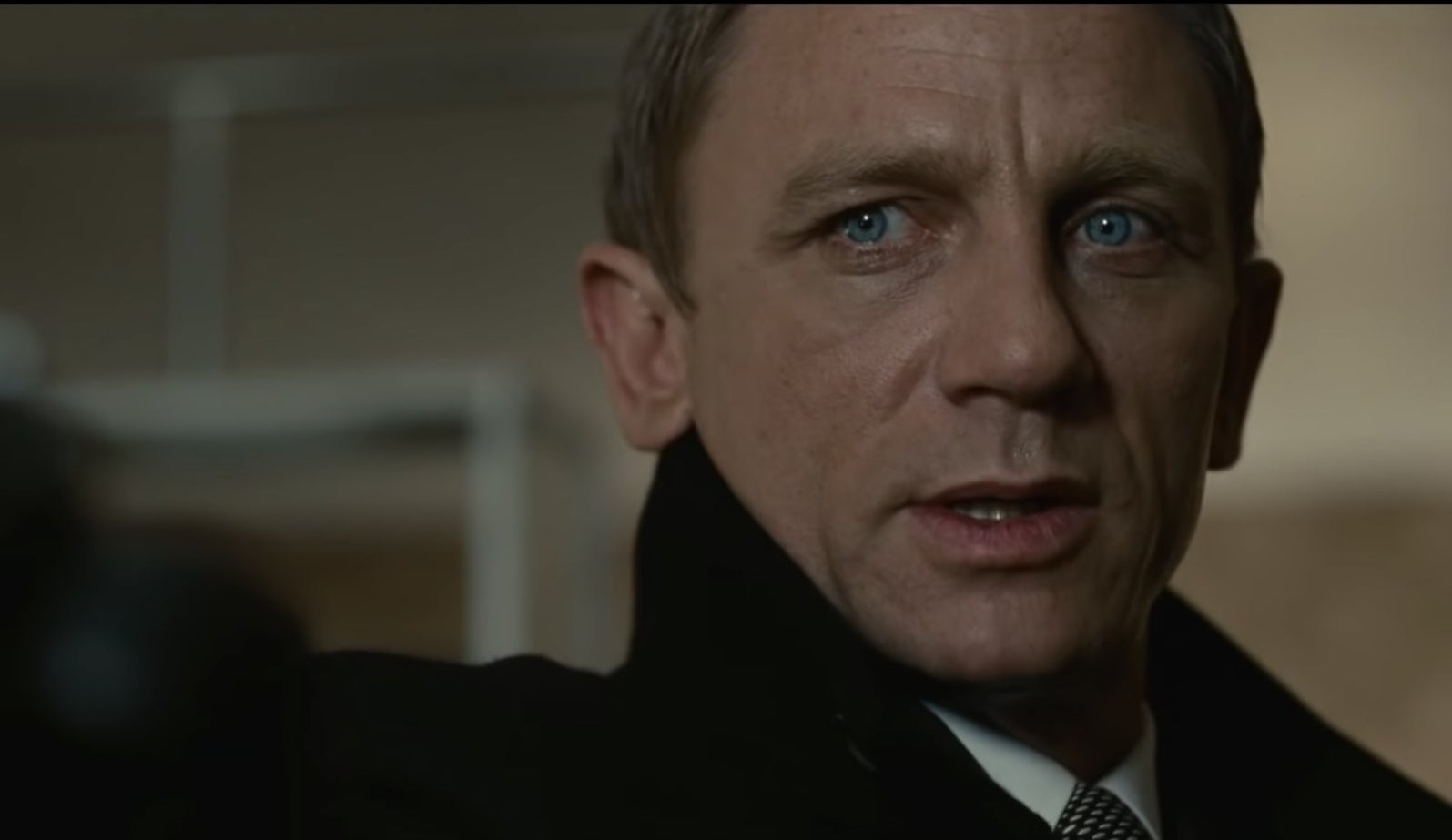 Daniel Craig in a black trench coat looks off-screen.