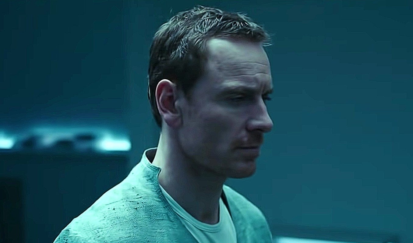 Michael Fassbender in a gray shirt looking pensive, and staring off-camera.