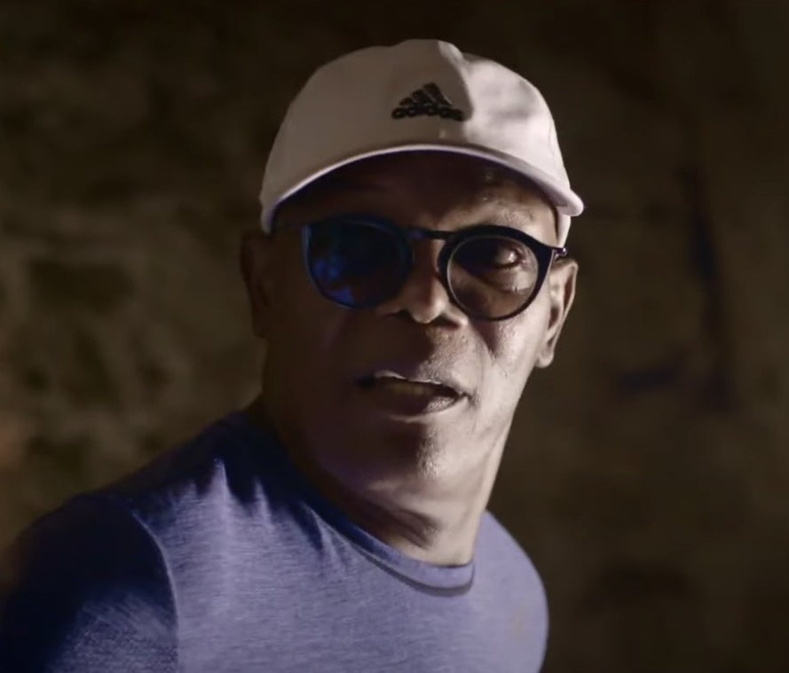 Samuel L. Jackson in sunglasses, a baseball cap, and a purple shirt.