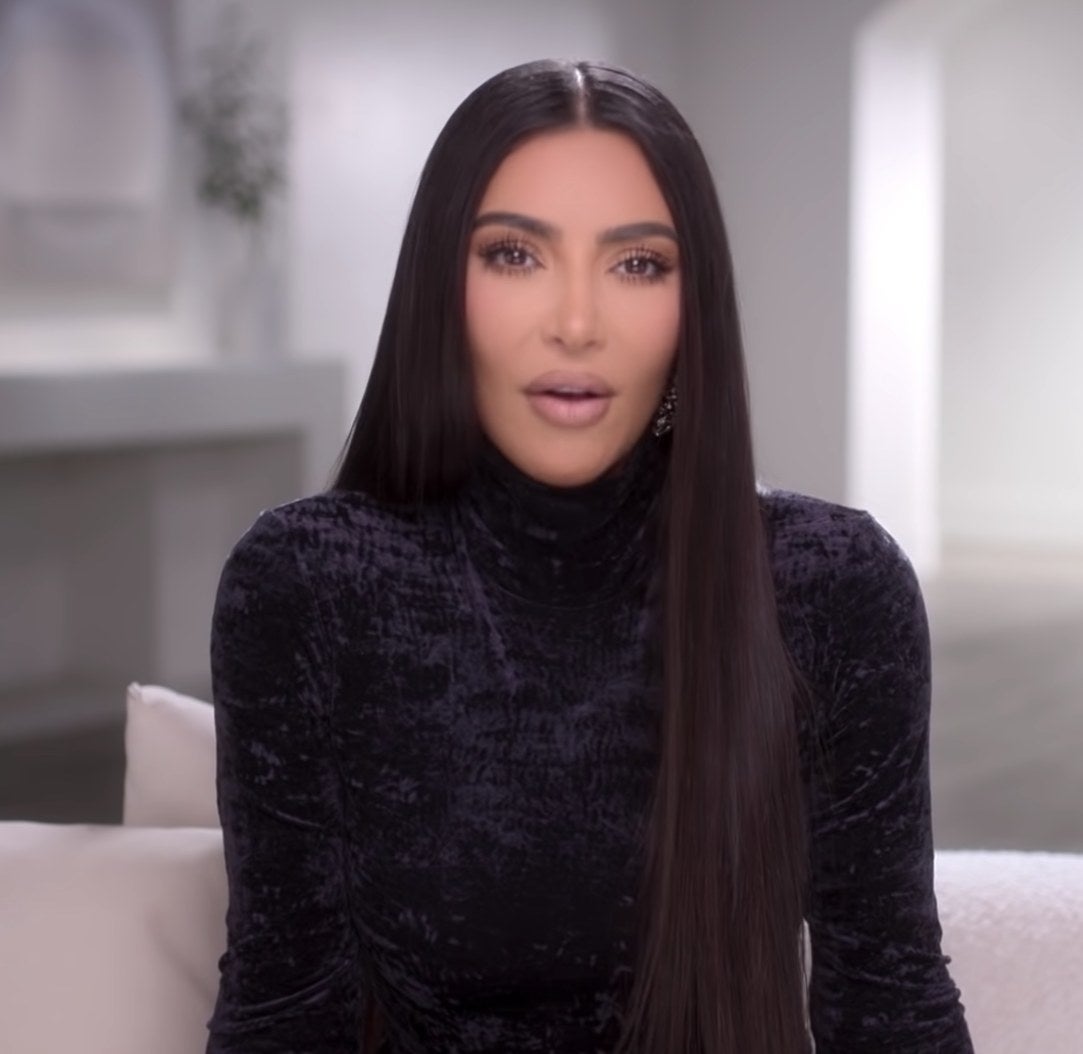 Kim Kardashian in a black velvet dress talks straight to the camera.