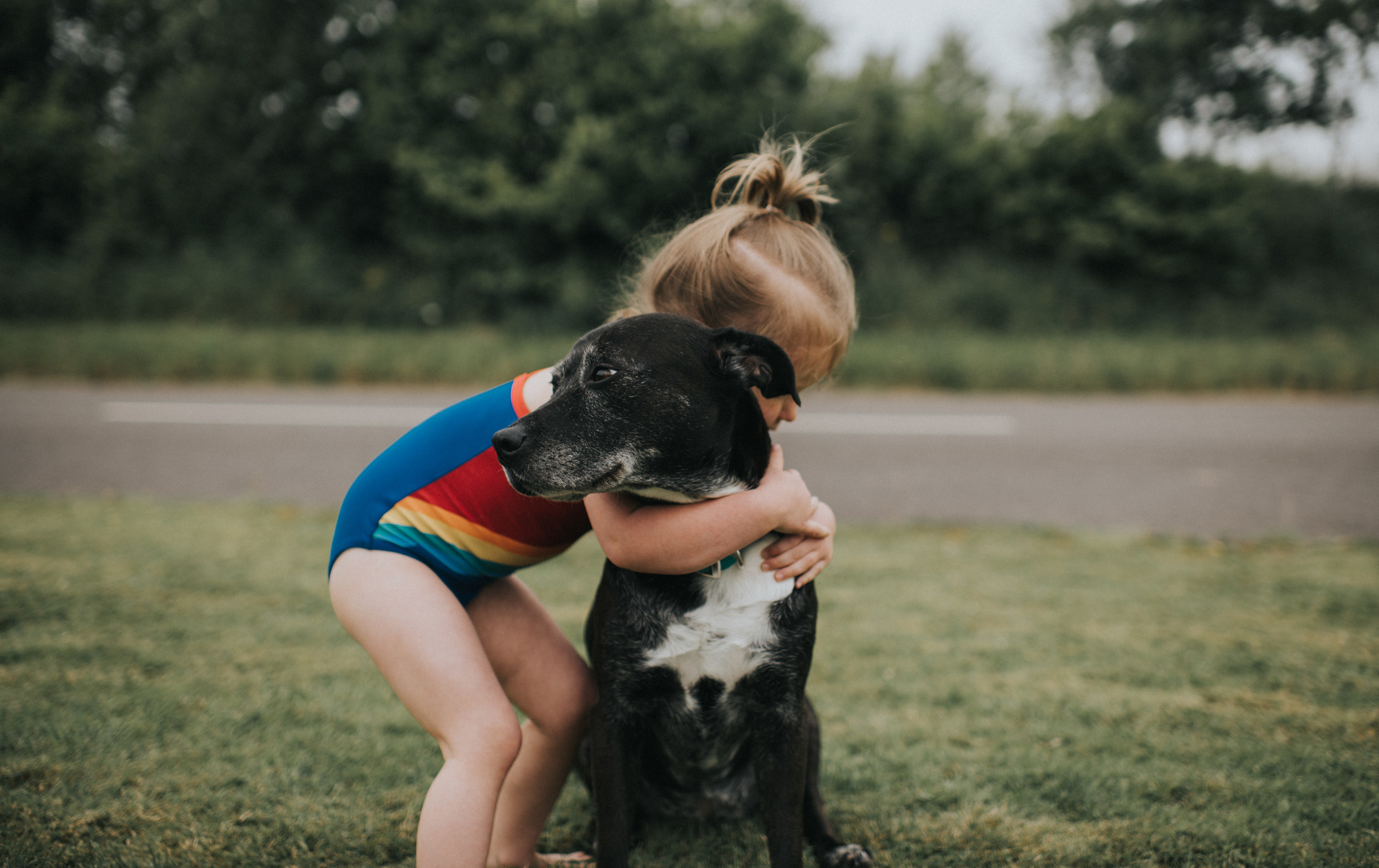 A young girl hugging a black dog.