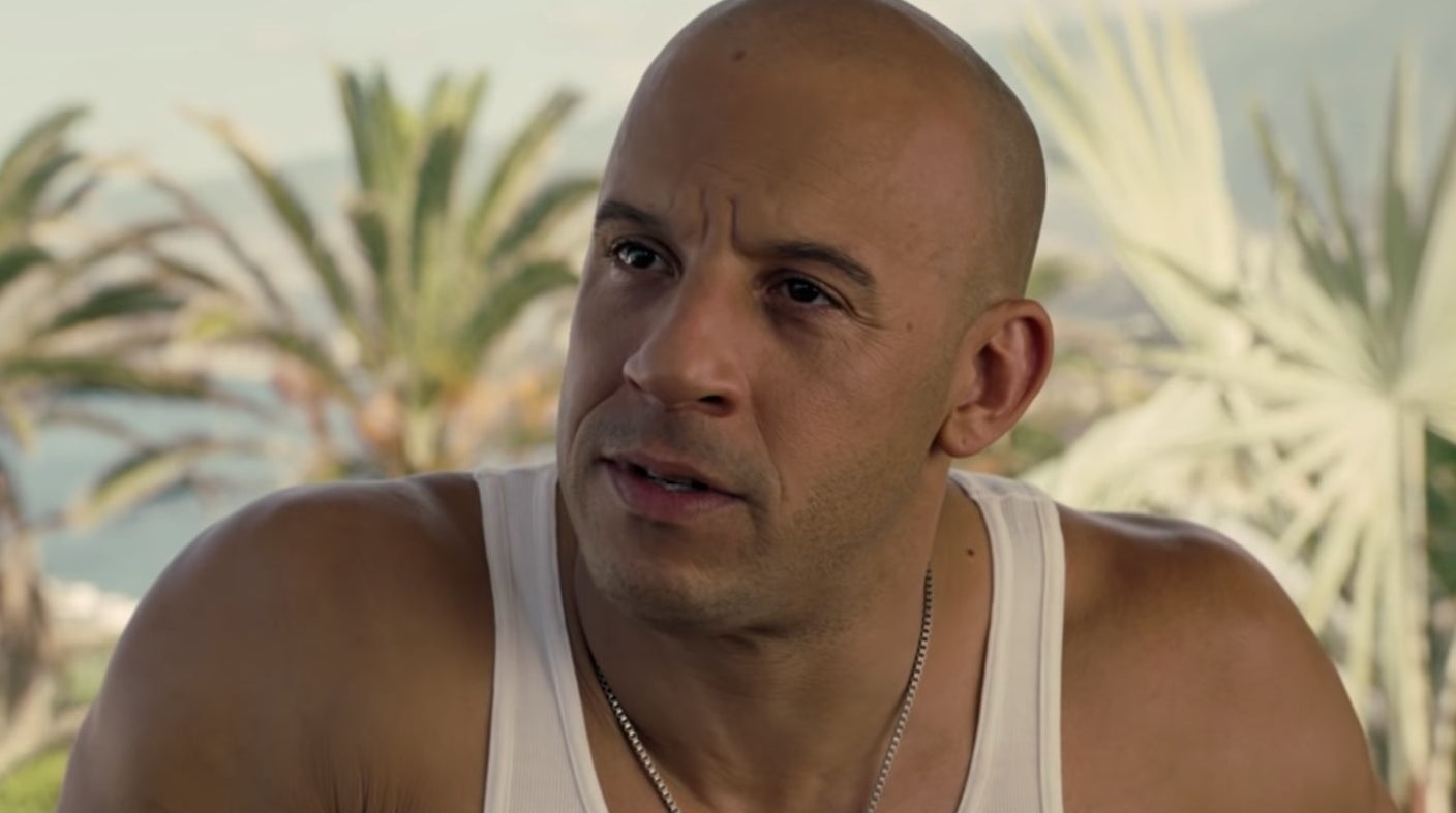 Vin Diesel in a white tank top and a silver necklace looks off-camera.