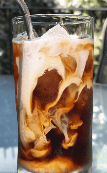 GIF of cream slowly spreading through iced coffee in a glass
