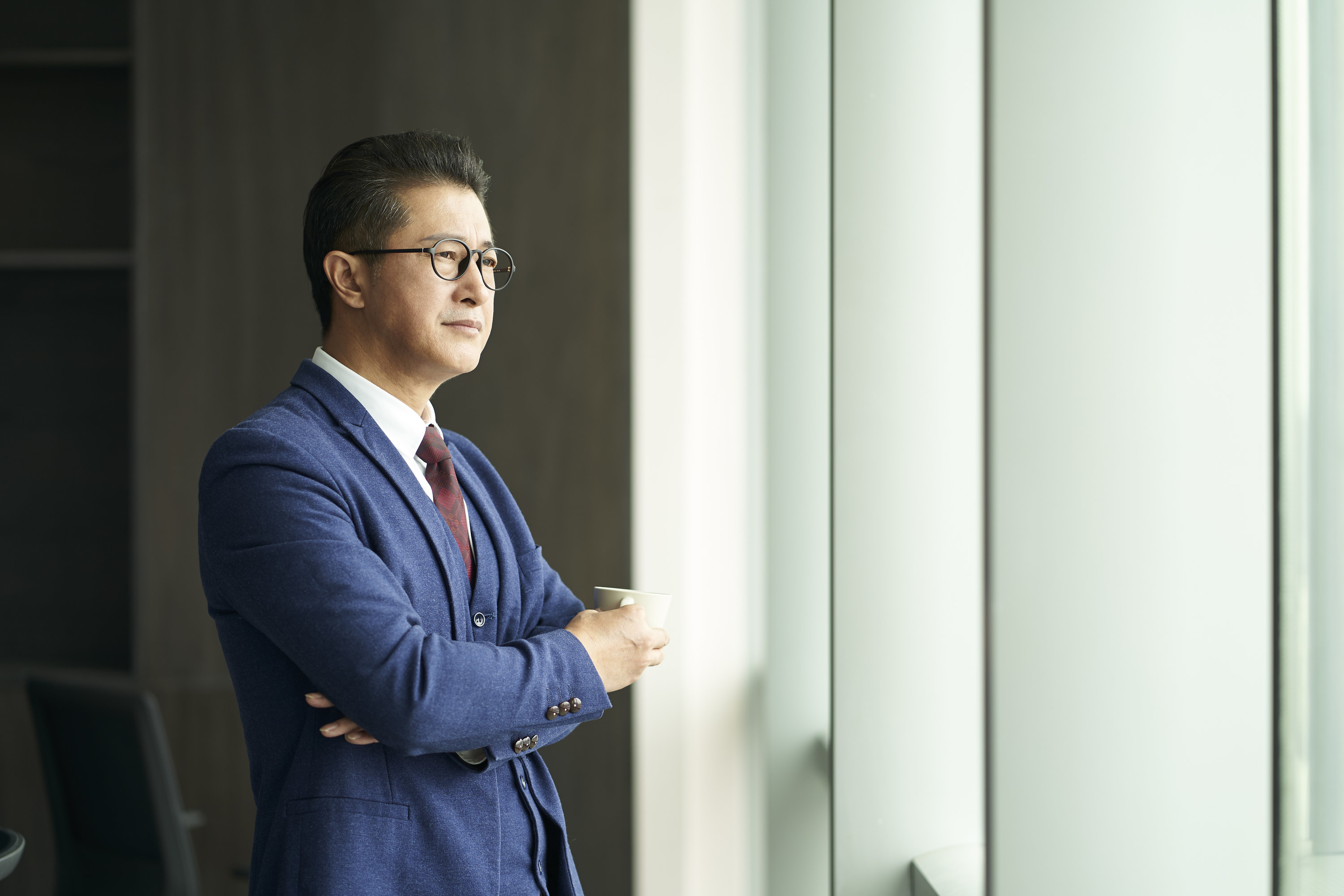 portrait of a asian business leader senior manager standing by window thinking