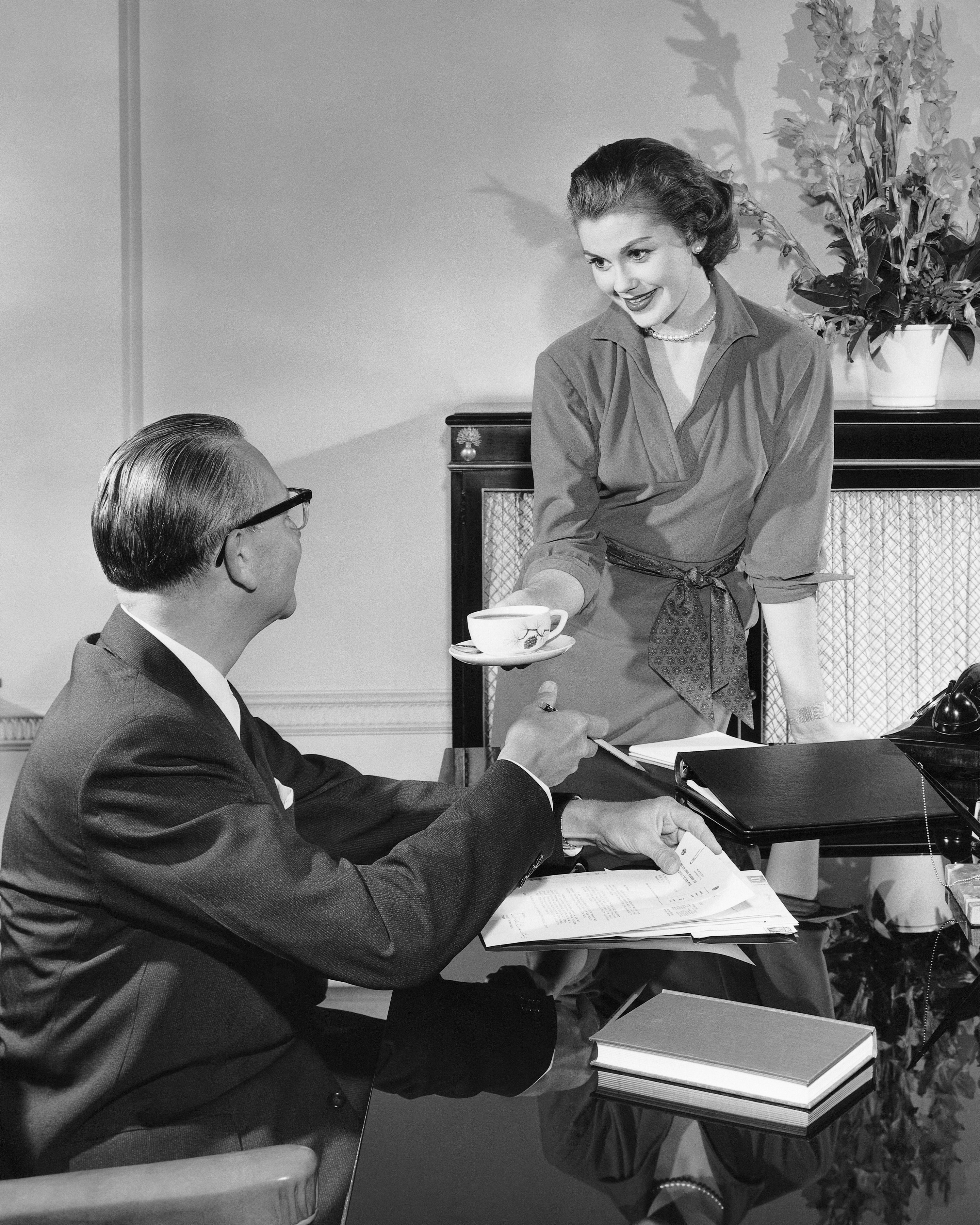 a woman serving a man a cup of tea at his desk