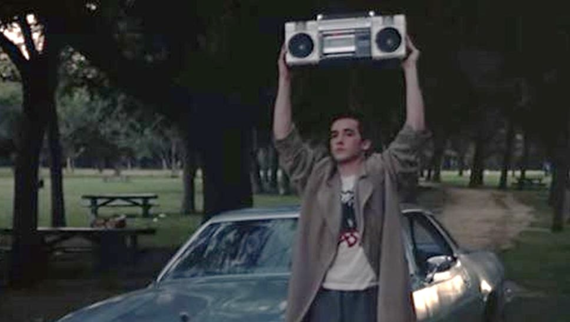 John Cusack standing outside a window holding a stereo system in a scene from Say Anything