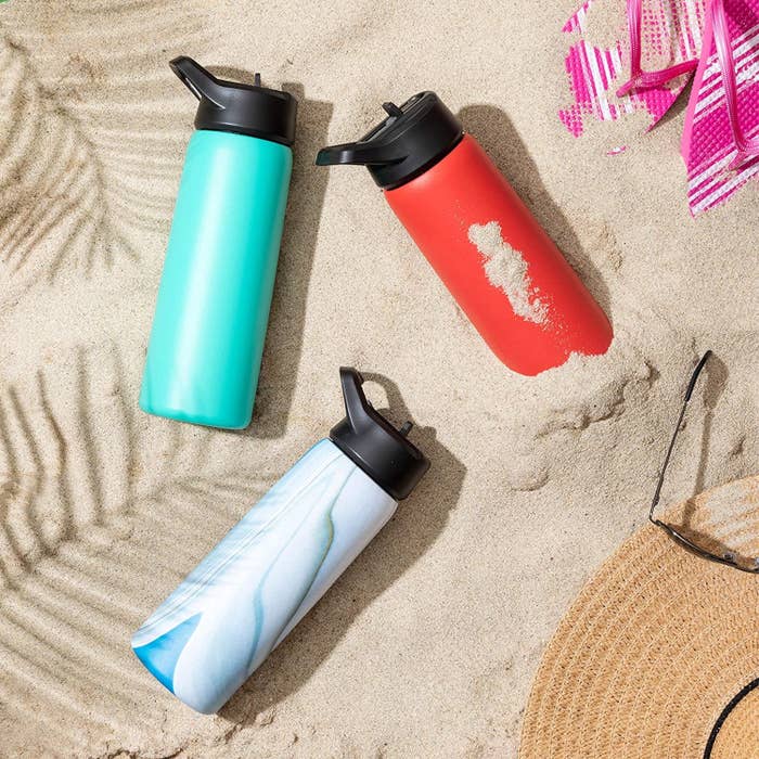 Three water bottles in the sand surrounded by beach accessories