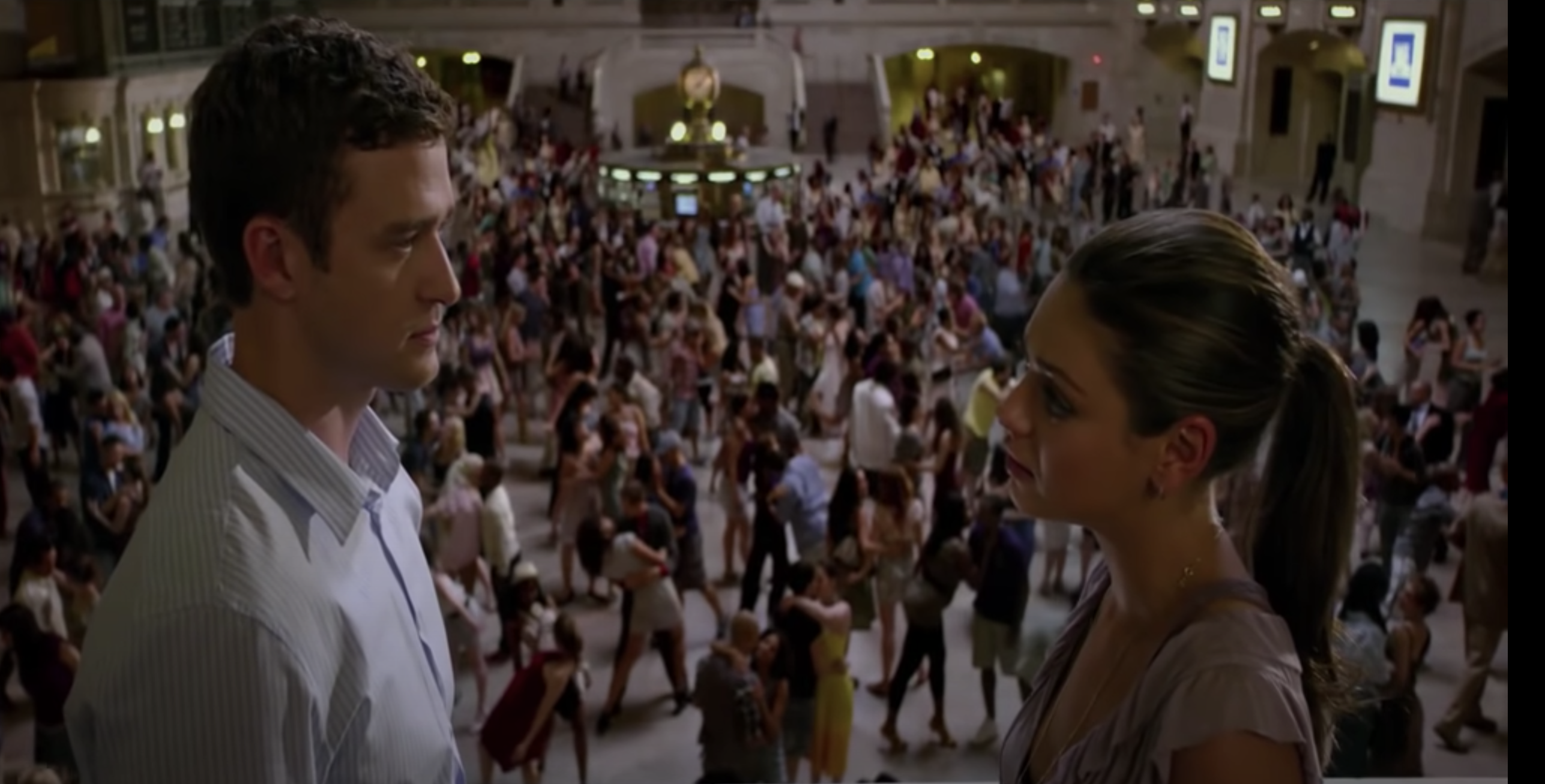 Justin Timberlake and Mila Kunis facing each other in front of a busy crowd in Friends with Benefits