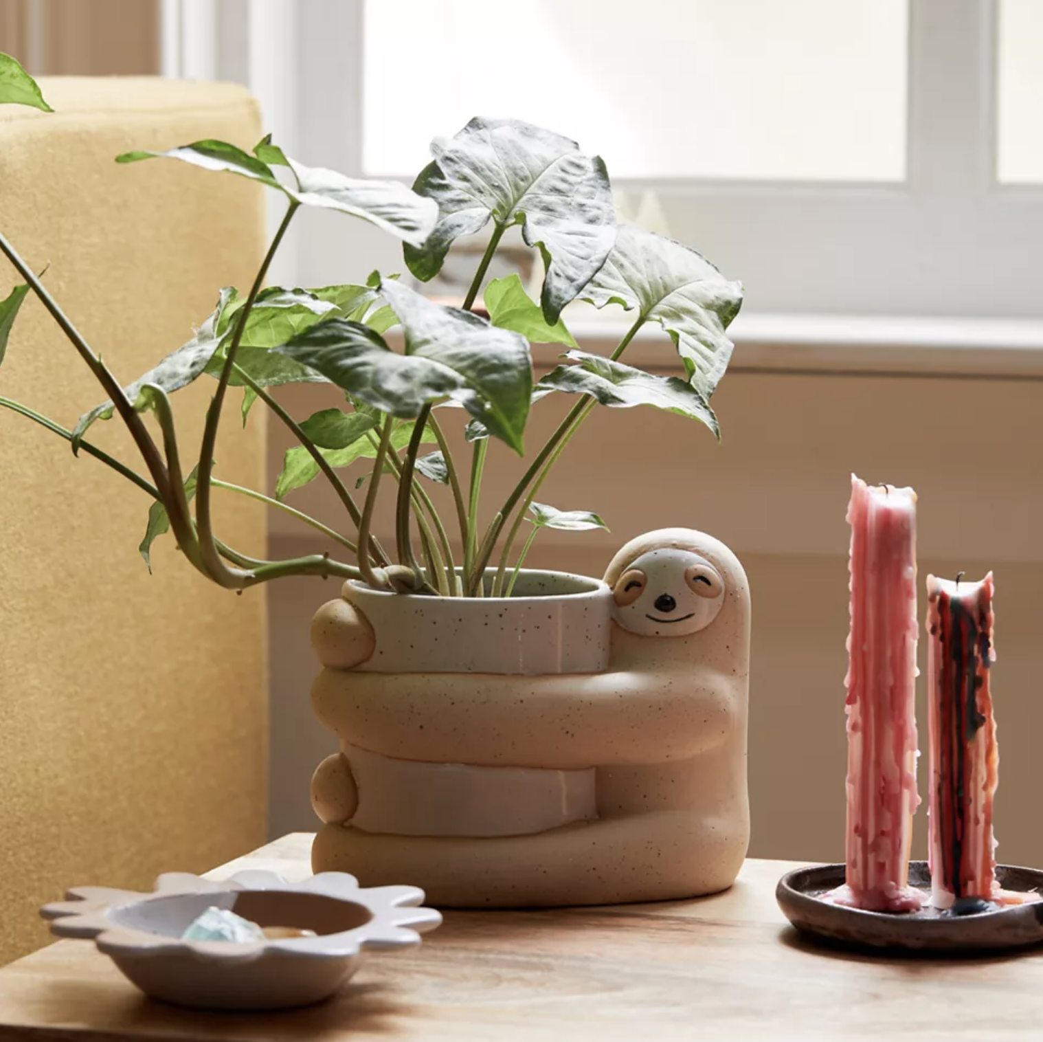 The sloth planter on a table surrounded by candles and a dish