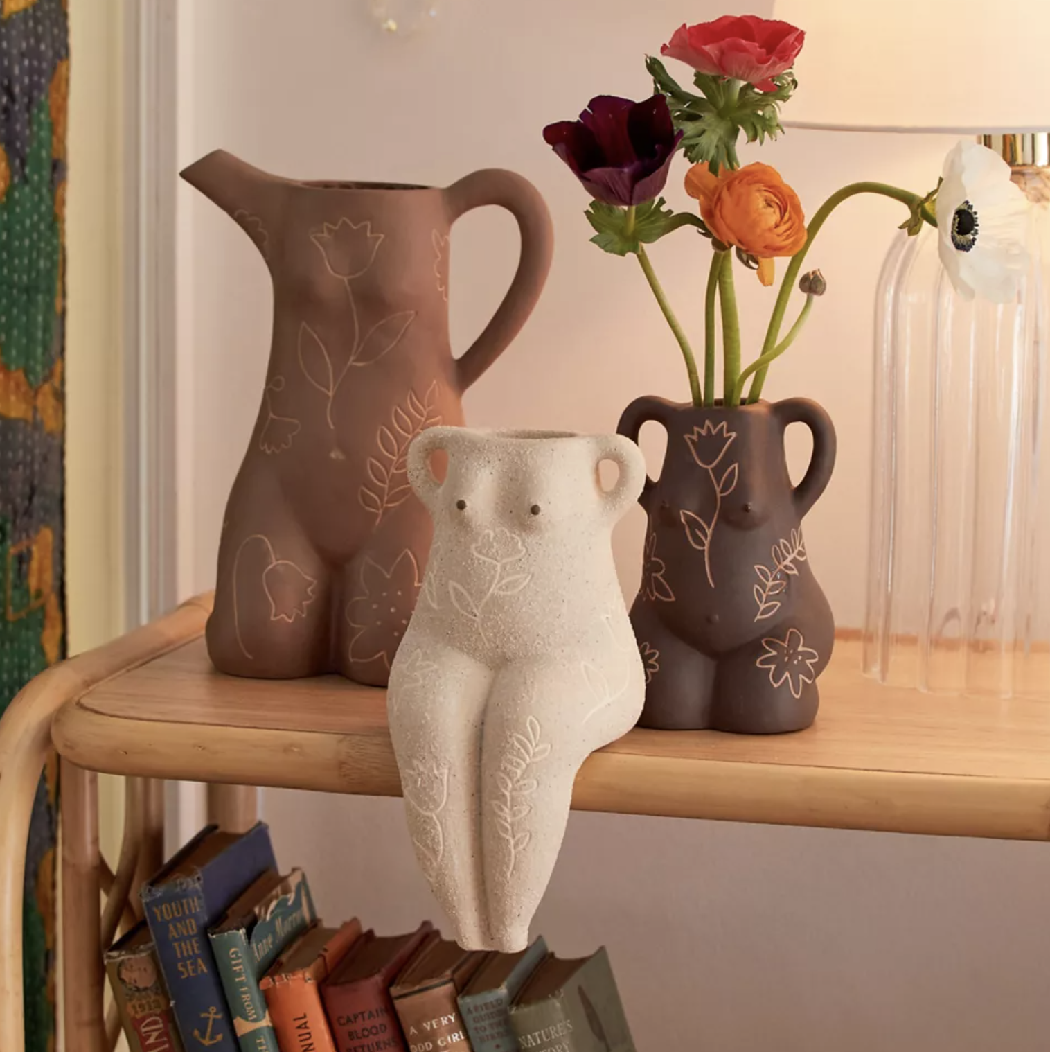 Three vases on a bookshelf, one has flowers in it