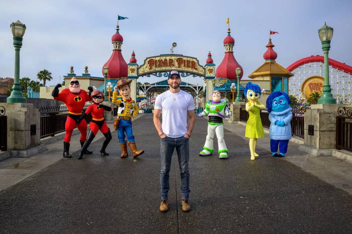 Chris standing in front of Mr. Incredible, Elastigirl, Woody, Buzz Lightyear, and Joy and Sadness in front of Pixar Pier