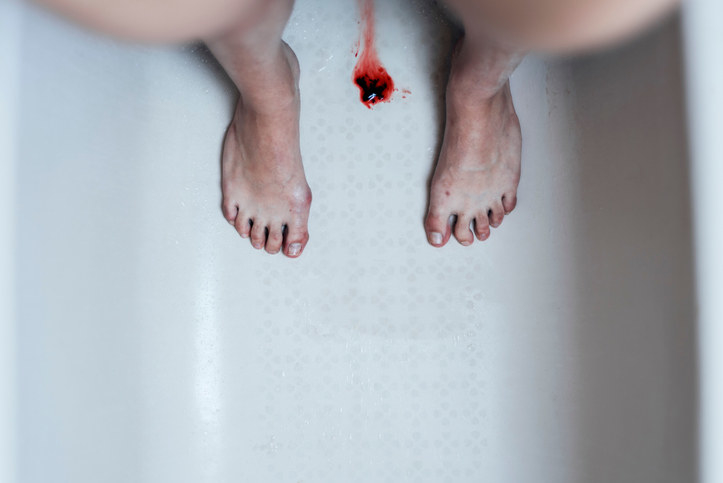 Person standing in a tub with a small patch of blood and a blood clot on the bottom of the tub