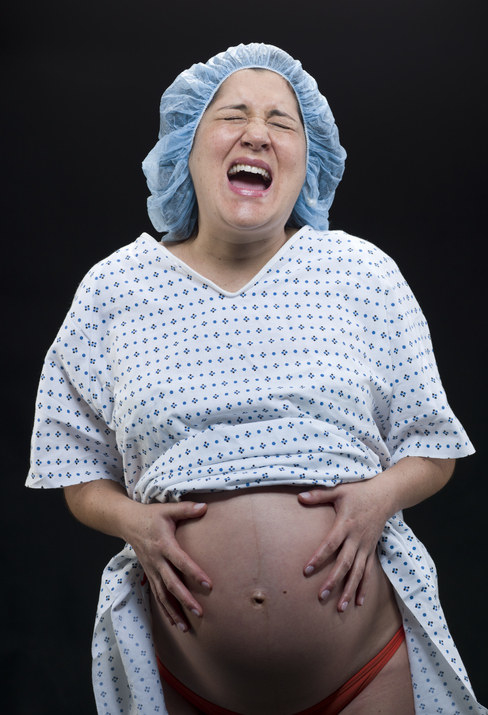 A pregnant person in a hospital gown screaming in pain