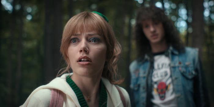 a character looking scared in the woods with a teenage guy behind her