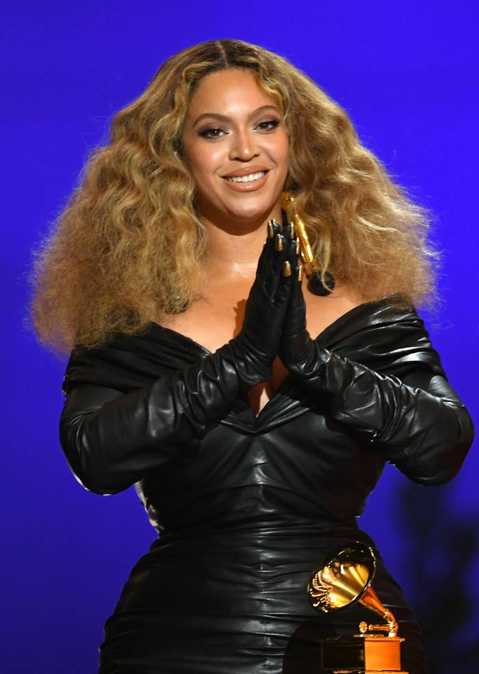 Bey accepting a Grammy award while wearing a leather-like form-fitting dress with matching opera-length gloves