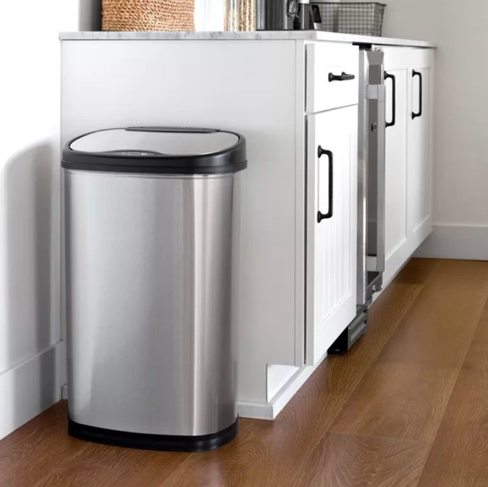Stainless steel trash can next to white kitchen cabinets