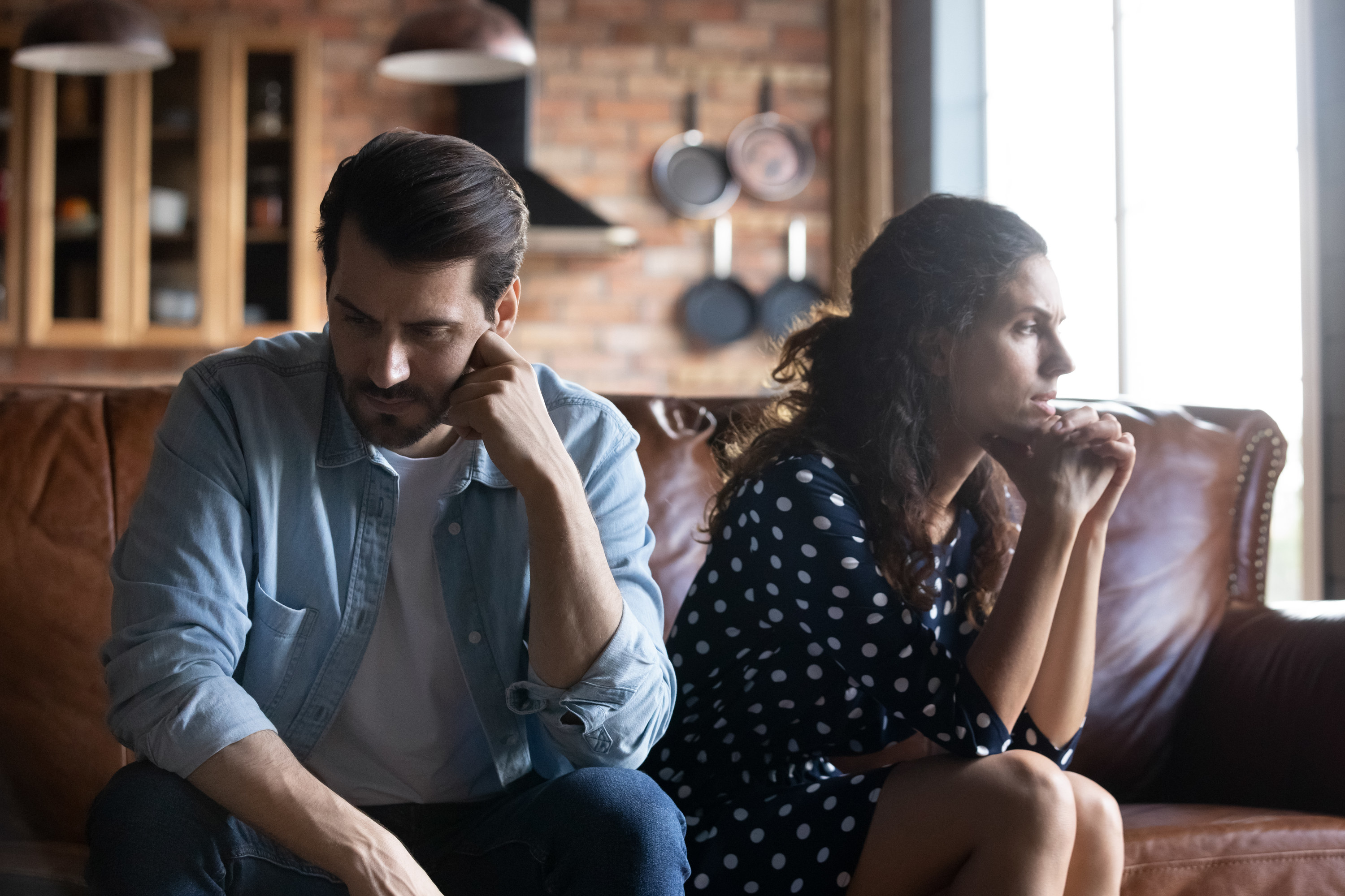 A man and woman sitting on a couch, not looking at one another.