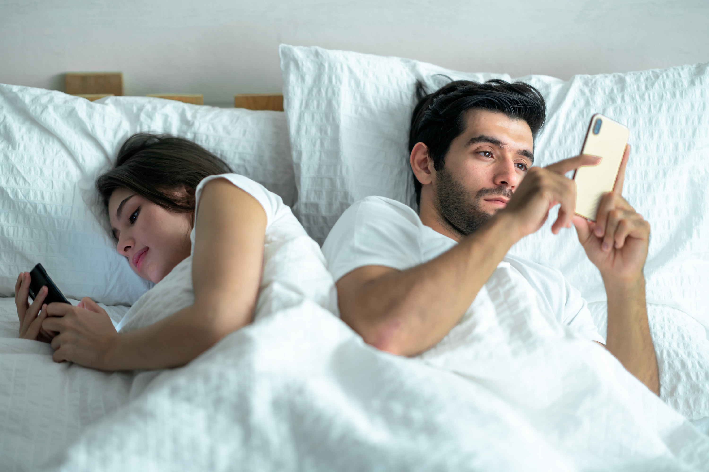 A man and woman laying in bed, each on their cell phones.
