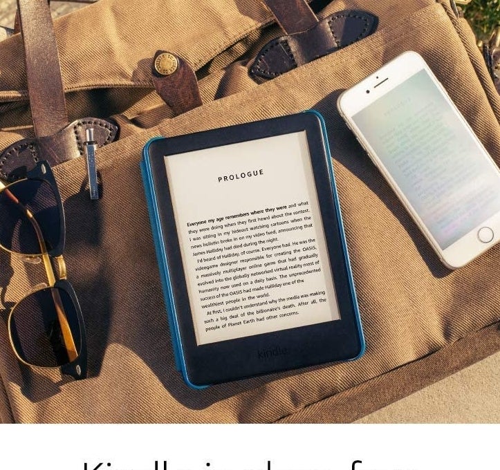 A Kindle on a bag beside sunglasses and a phone