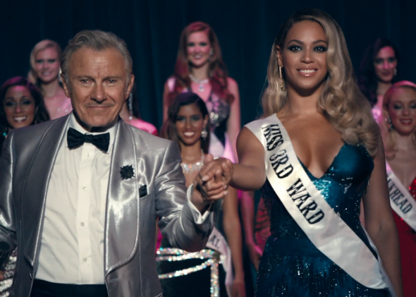 Beyonce stands on a stage in front of a row of other women, she&#x27;s wearing a ballgown and a sash that reads &#x27;Miss 3rd Ward&#x27;, and is holding hands with a man in a hux