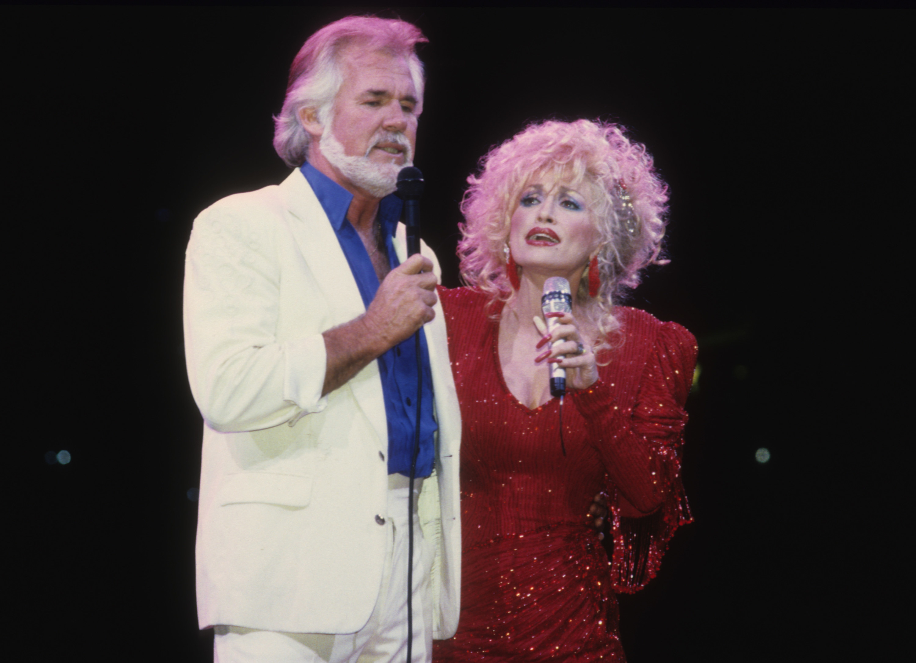 Kenny Chesney, in a white suit, and Dolly Parton, in a glittery red dress, sing together on stage