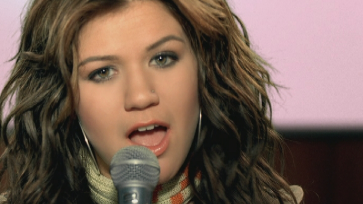 Kelly Clarkson looks into the camera and sings into a microphone