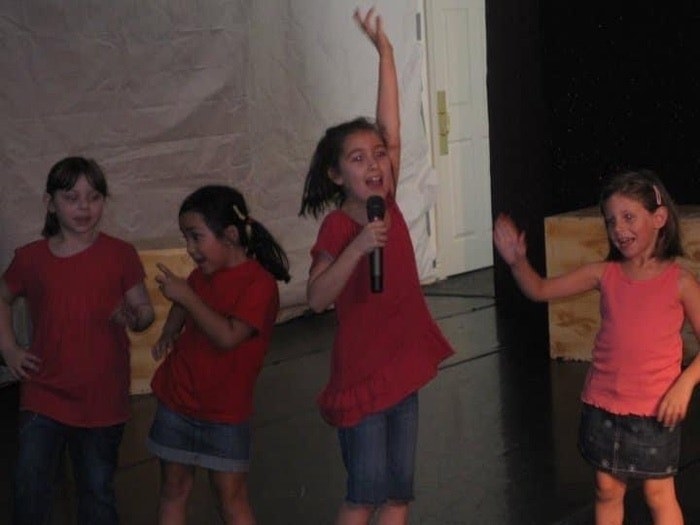 young girl singing into a mic with friends dancing behind