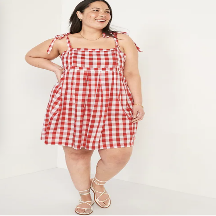 A person wearing a gingham dress in front of a plain backdrop