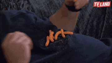 Kevin James on a couch eating cheetos with his mouth open