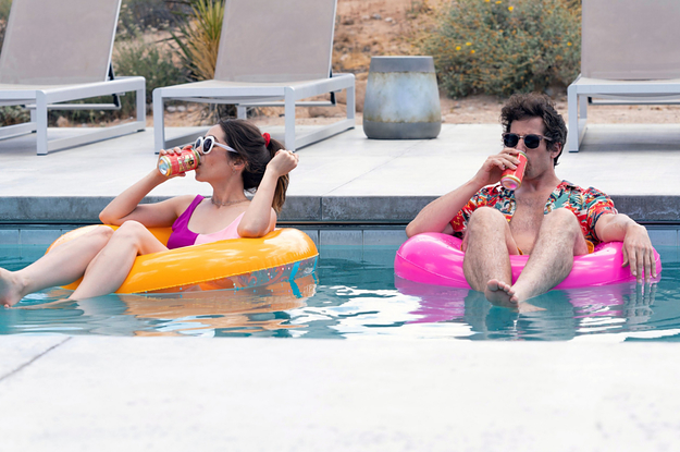 Christin Miloti and Andy Samberg sit in a pool in inner tubes drinking something out of cans as Sarah and Nyles in Palm Springs