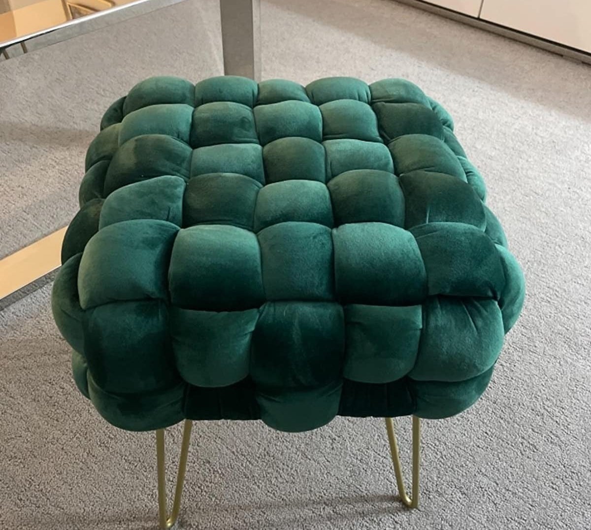 a reviewer photo of the emerald green velvet ottoman with gold hair pin legs on a rug