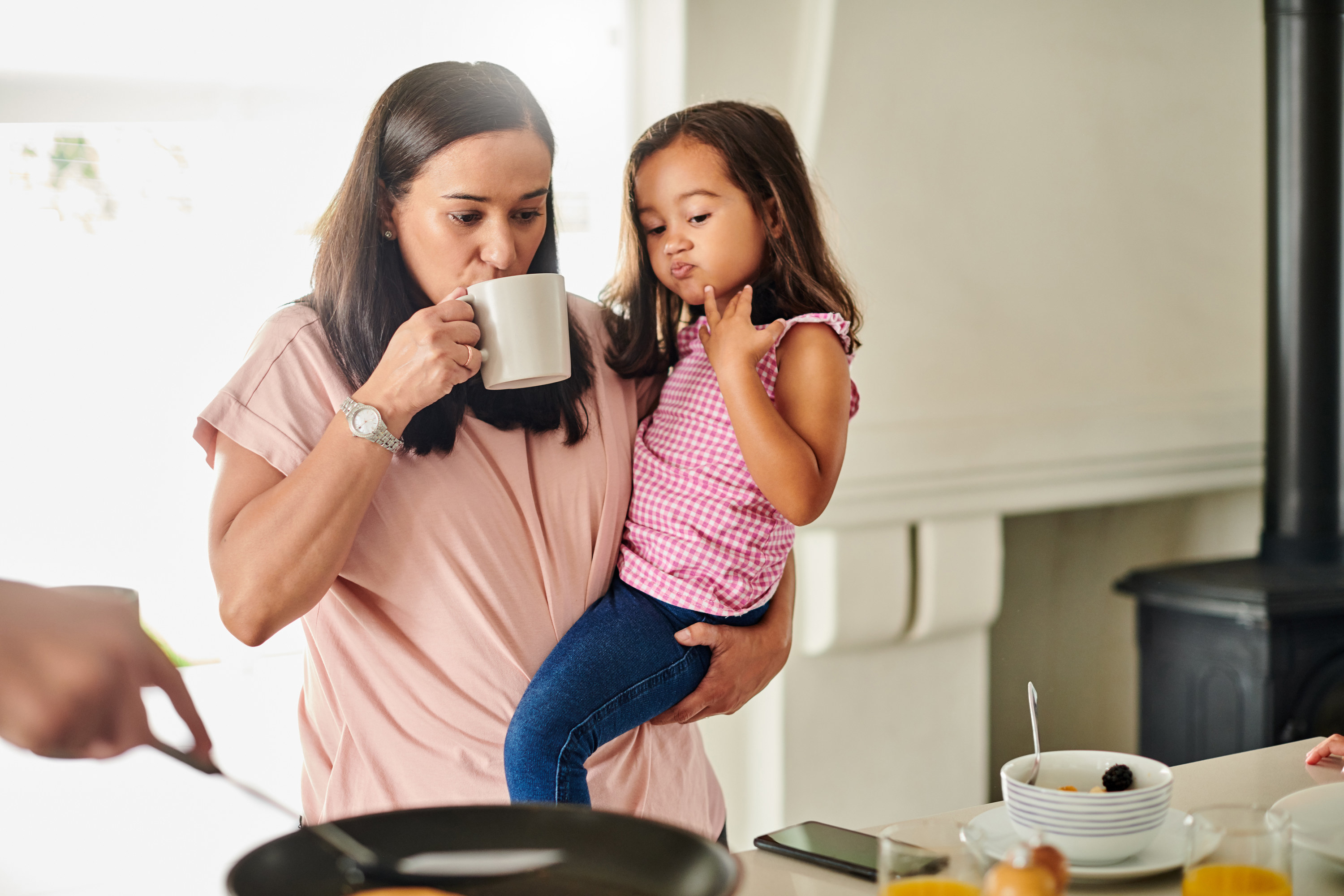 A woman holds her daughter and drinks coffee
