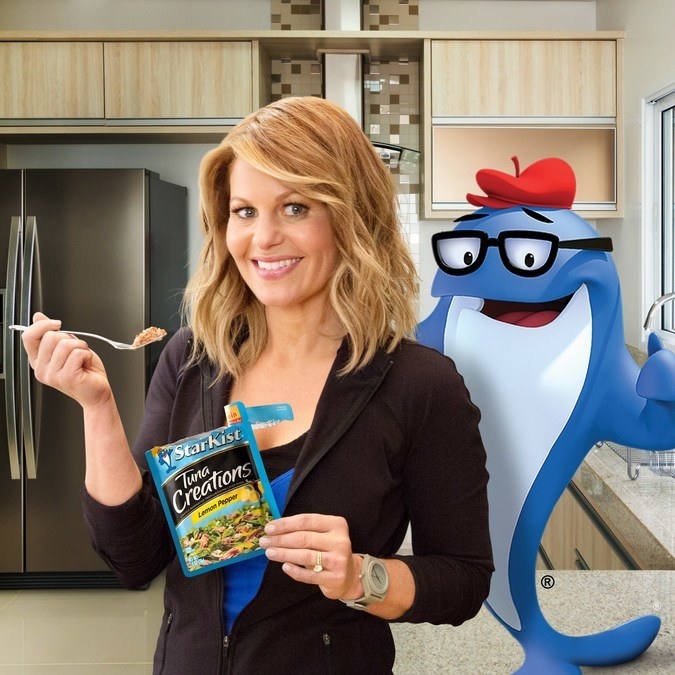 Candace Cameron Bure stands in a kitchen, eating tuna with a fork out of a StarKist pouch, and there&#x27;s a cartoon shark next to her