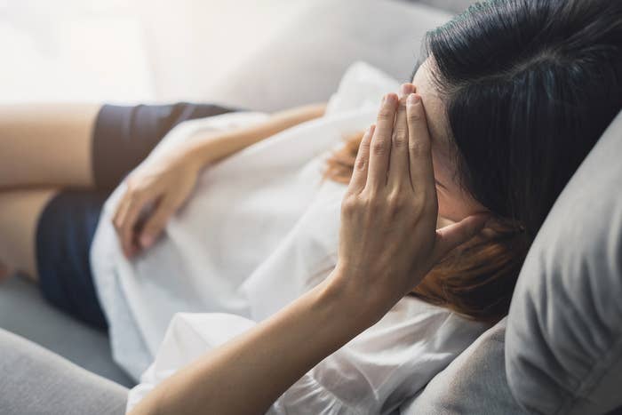 A woman sits on a couch while holding her head