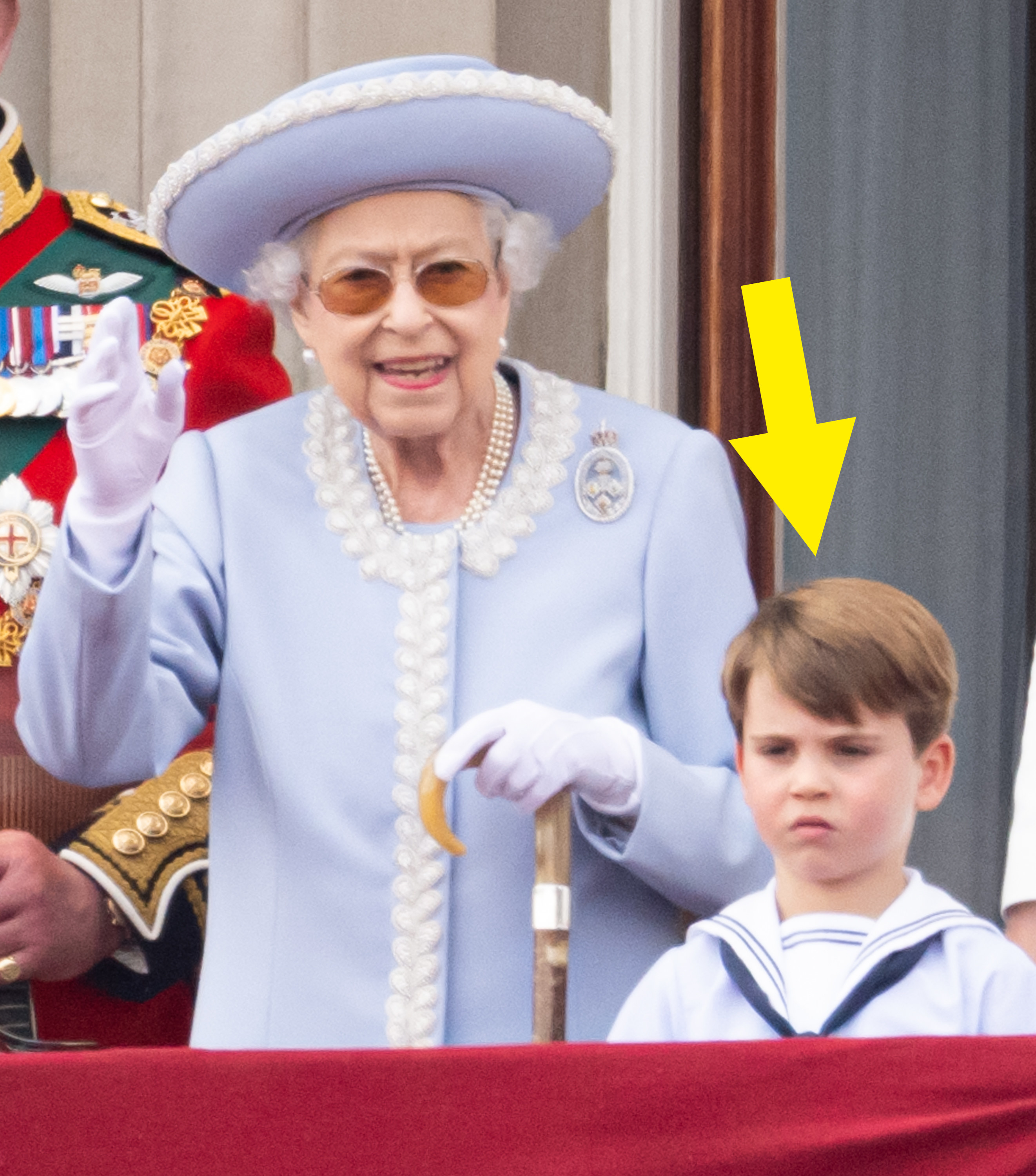 An arrow points to Prince Louis, who looks bored and annoyed standing next to Queen Elizabeth