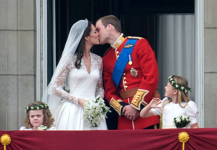 Prince William in an ornate uniform kisses Kate Middleton in a wedding dress, while two young girls hold flowers on either side of them