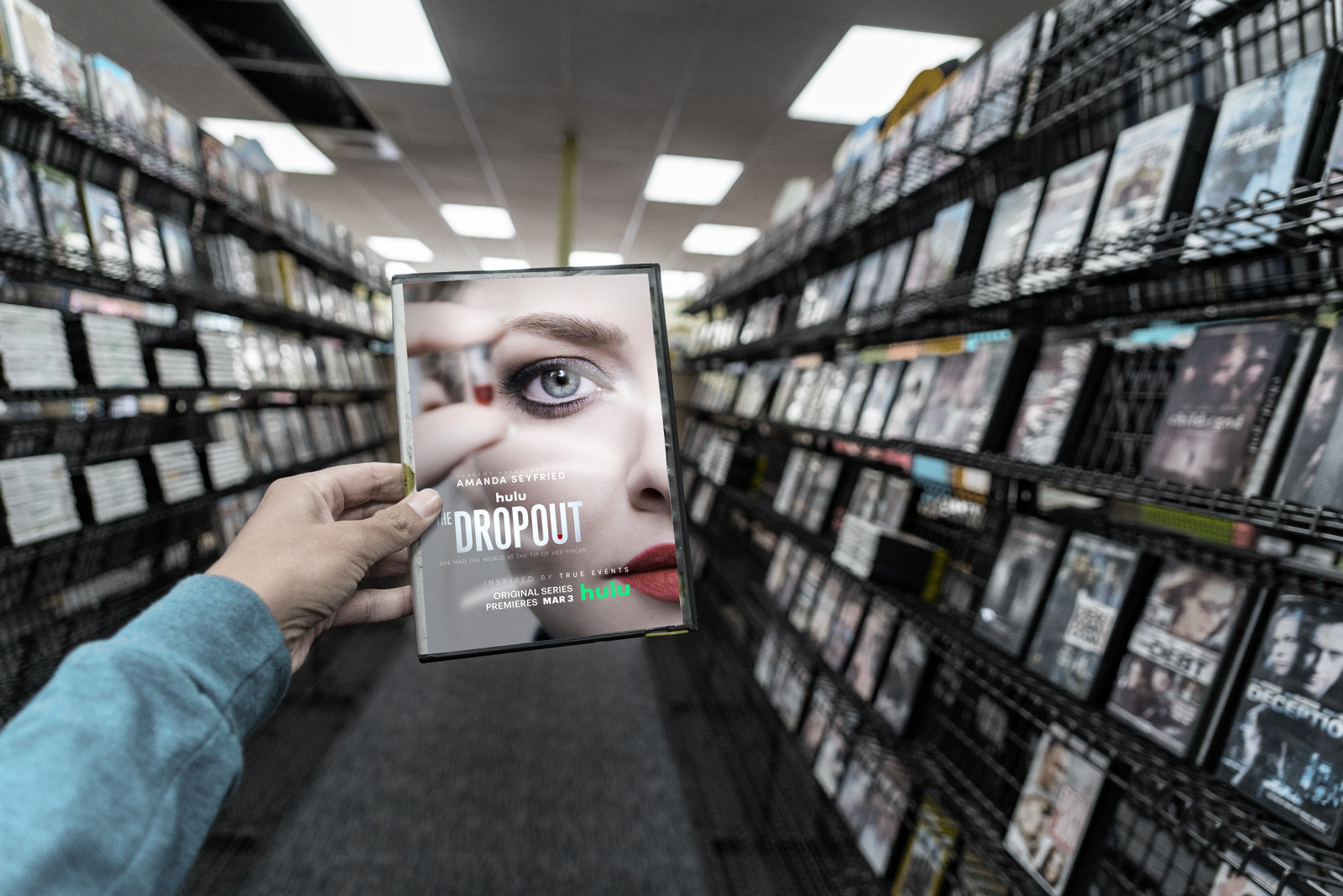 A photo illustration of a man holding a DVD copy of The Dropout in a Blockbuster store