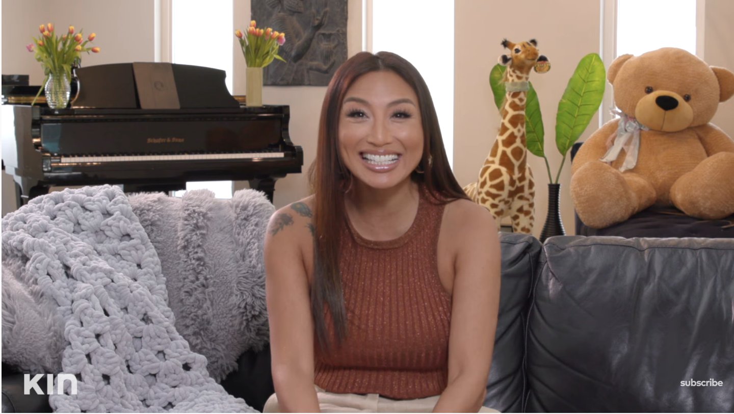 Jeannie Mai smiling and sitting on a couch