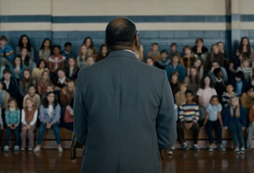 A school gym with a teacher talking to the kids