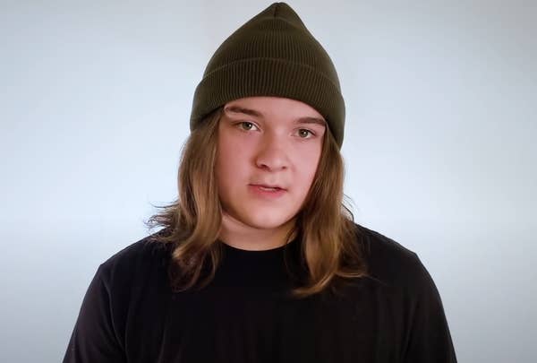 Young person with shoulder-length hair and wearing a cap