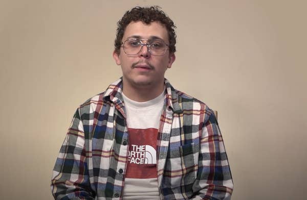 Man with glasses and a small mustache and wearing a \"The North Face\" T-shirt and plaid jacket